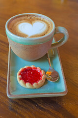 coffee cup with heart shape with strawberry biscuit on blue plate