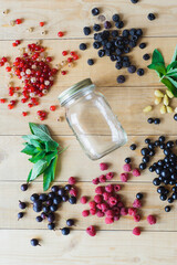 Red, white, black currant, red and black raspberries, white strawberries and mint leaves with glass jar on wooden table as ingredient to healthy cocktail, beverage, yogurt, smoothie