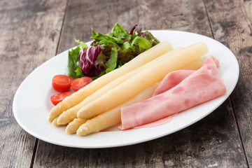 White asparagus with salad and ham on wooden background
