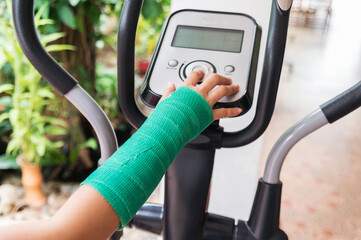 green cast on hand and arm touching exercise bike at home, body injury concept