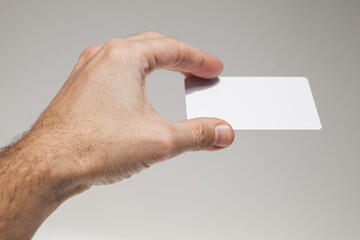 Fototapeta premium Male hand with white empty card on gray wall