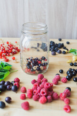 Red, white, black currant, red and black raspberries, white strawberries and mint leaves with glass jar on wooden table as ingredient to healthy cocktail, beverage, yogurt, smoothie
