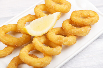 Close-up of a plate of squid a la romana next to a beer on white wooden table. Food squids. Horizontal shoot.