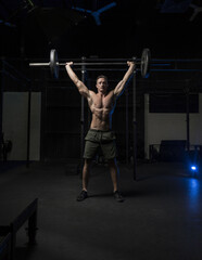Fototapeta na wymiar Muscular White Caucasian man does a barbell overhead press in a dark grungy gym wearing shorts and showing muscular body 