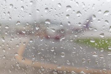 Rain drops on airplane window glass and blurred airport runway in background.