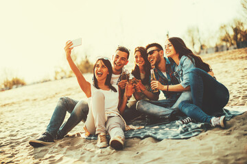 Happy young people having fun on the beach drinking beer and doing selfie