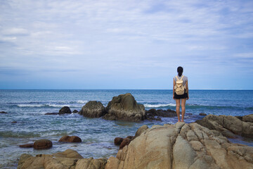 Lonely girl stand on the rock beach and looking to the sea