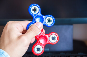 Man's hand holds two multi-colored spinners on the background of a personal computer close-up