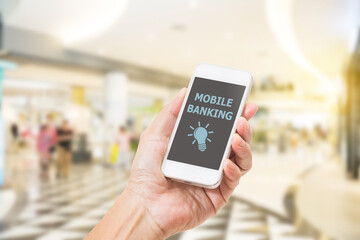 Hands holding mobile phone with Mobile banking word on screen. blurred image of shopping mall background