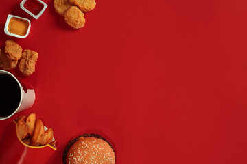 Concept of mock up burger, potatoes, sauce, chicken nuggets and drink on red background. Copy space for text and logo.