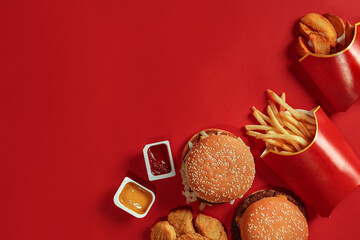 Two hamburgers and french fries, sauces on red background. Fast food. Top view.