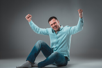 Appealing casual young man sitting on the floor, looking to the camera smiling
