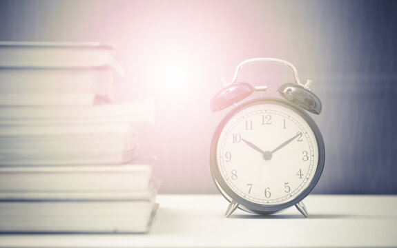 Vintage clock and stack of books time at 10 minute pass ten with retro flare light color effected from backside