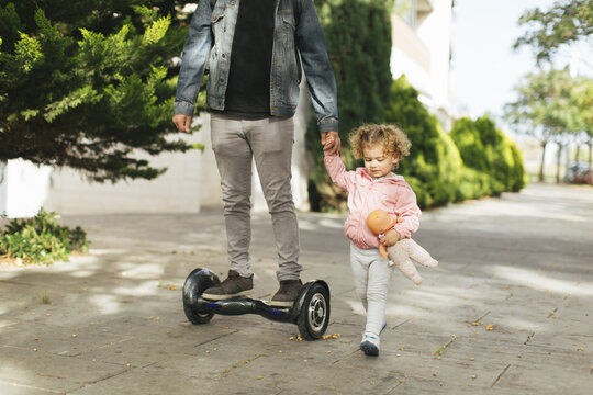 Father on hoverboard hand in hand with his little daughter on pavement