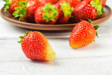 Fresh organic strawberries on white wooden planks and full plate with strawberries on the background, close-up, selective focus