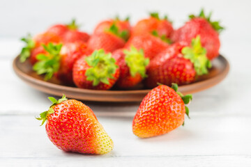 Fresh organic strawberries on white wooden planks and full plate with strawberries on the background, close-up, selective focus