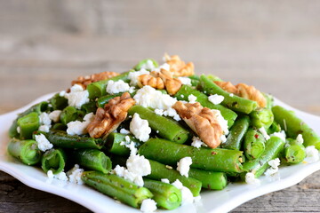Spicy green bean salad recipe. Baked green beans salad with cottage cheese, crunchy walnuts, garlic and spices on a plate and a vintage background. Simple vegetarian bean salad. Closeup