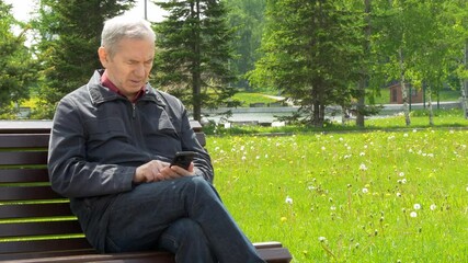 Elderly Man Sitting On Park Bench And Using Mobile Phone
