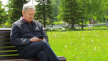Elderly Man Sitting On Park Bench And Using Mobile Phone