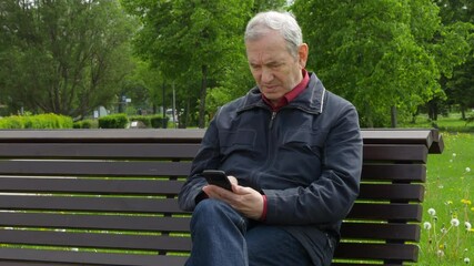 Elderly Man Sitting On Park Bench And Using Mobile Phone