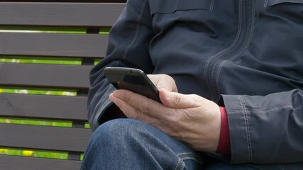 Elderly Man Sitting On Park Bench And Using Mobile Phone