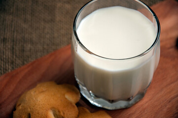 A glass of milk with cookies on a wooden board on a background sacking Copy space. Space for text.