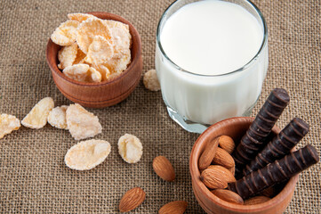 A glass of milk with almond nuts, corn flakes, chocolates,  on sacking background