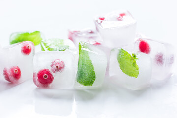 frozen red berries in ice cubes with mint on stone background