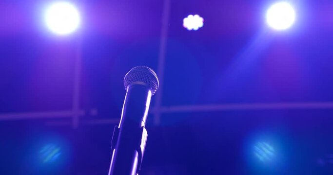 Bluish violet lights shine on to a microphone. There is no performer present and as the lights shift the stage and equipment are illuminated by their beautiful colors.