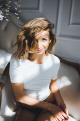 Naklejka premium close-up portrait of a beautiful slim sexy cute girl on a bed with white linen in white top blond wake up and stretches and smiles