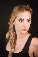 Fototapeta premium ritratto di bellissima ragazza bionda con la coda a treccia vestita di una canotta nera che guarda lontano - sfondo nero