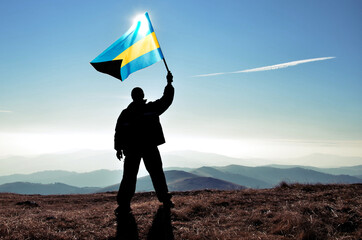 Successful silhouette man winner waving Bahamas flag on top of the mountain peak