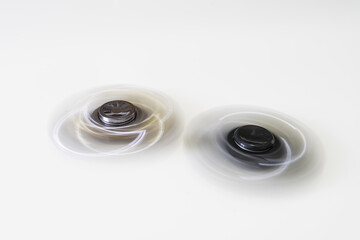 Long exposure with motion blur of two fidget spinners during fast rotation on a white background.