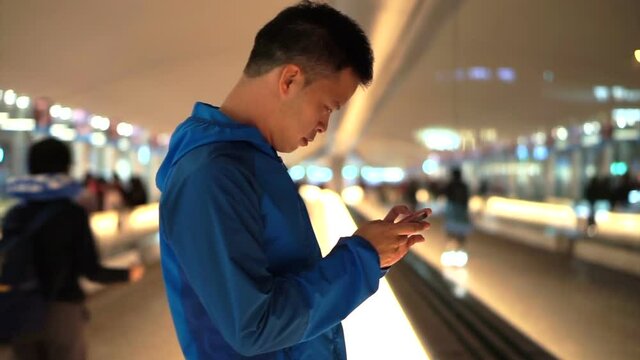Asian backpacker man checking using smart phone at airport after landing at night