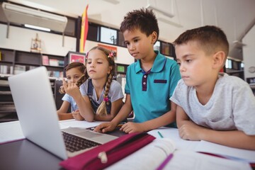 Attentive schoolkid using laptop in library