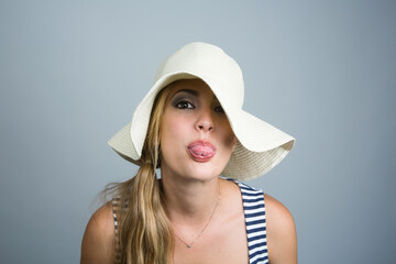 bella ragazza con canotta a righe e cappello bianco fa una linguaccia - sfondo grigio 