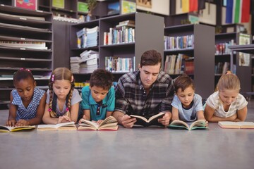 Teacher and kids lying on floor while reading books 