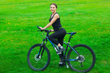 Naklejka premium Attractive young woman riding a mountain bike in a park on a green lawn in the spring.