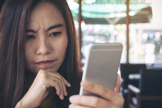 A Beautiful Asian Woman Looking At Smart Phone With Feeling Stress In Modern Cafe