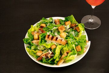 Chicken Caesar salad with rose wine on black background