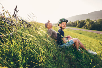 Father and son rest in high green grass after bicycle walk