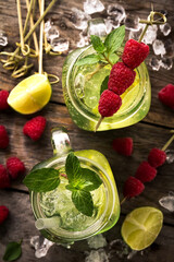 Tasty cold fresh drink lemonades with lemon, mint, raspberry, ice and lime in glass on wooden table. Top View.