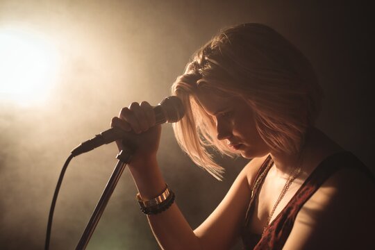 Confident female singer with microphone in illuminated nightclub