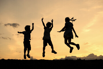 Fototapeta na wymiar Silhouettes of group of children jumping high joyfully on sunset background
