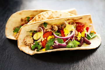 Beautiful tasty appetizing traditional mexican food tacos with meat and vegetables on black slate. Closeup.