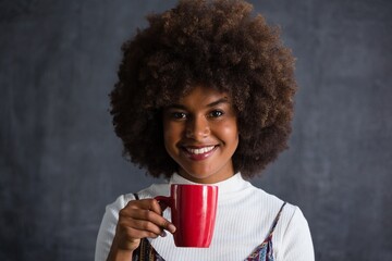 Smiling woman with frizzy hair holding coffee mug against wall - obrazy, fototapety, plakaty