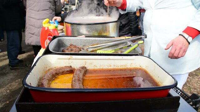sausages in a roasting tin and cooker who prepares them,, pig slaughter festival, Belo Blato, Vojvodina, Serbia, March 12, 2017.
