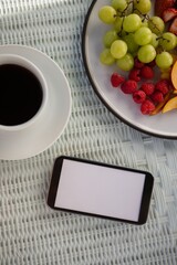 Overhead view of mobile phone by coffee cup and fruits