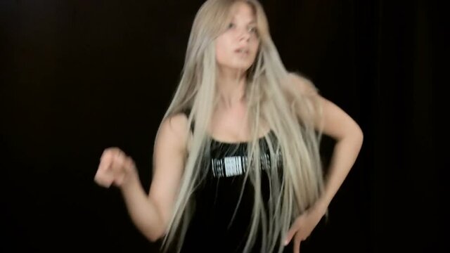 A blonde girl woman with very long hair dances go-go. Close-up. Separate movements. Slow motion. Loose hair. On a black background.