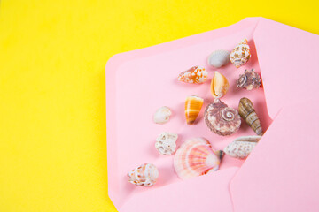 Fototapeta na wymiar Pink envelope with sea shells on colored yellow background, top view